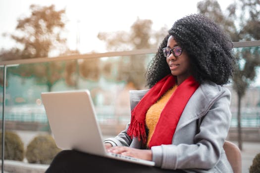 A woman working remotely on a laptop outdoors in a park setting. Stylish and focused.
